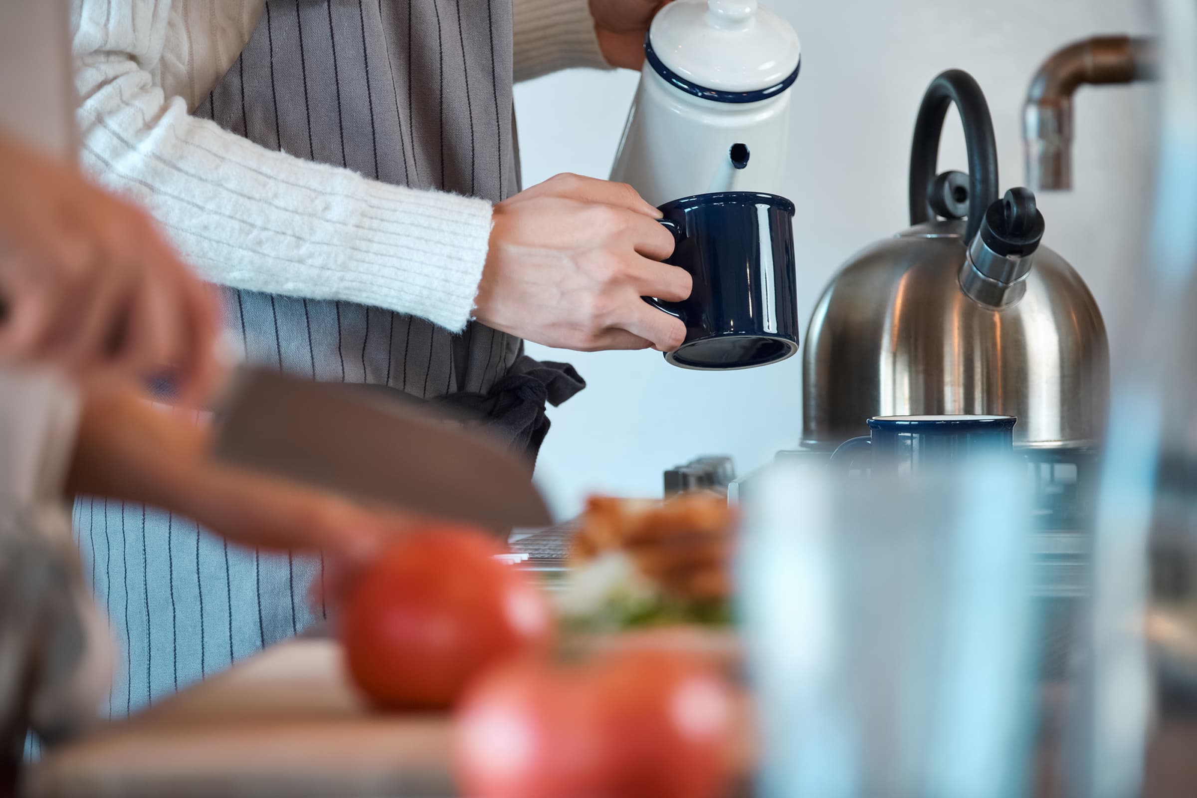 キッチンでケトルからコップにお湯を注いでいる様子の写真