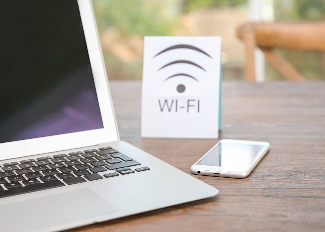 ノートパソコンとスマートフォン、Wi-Fiが利用可能であることを示すサインがテーブルに置かれている様子の写真