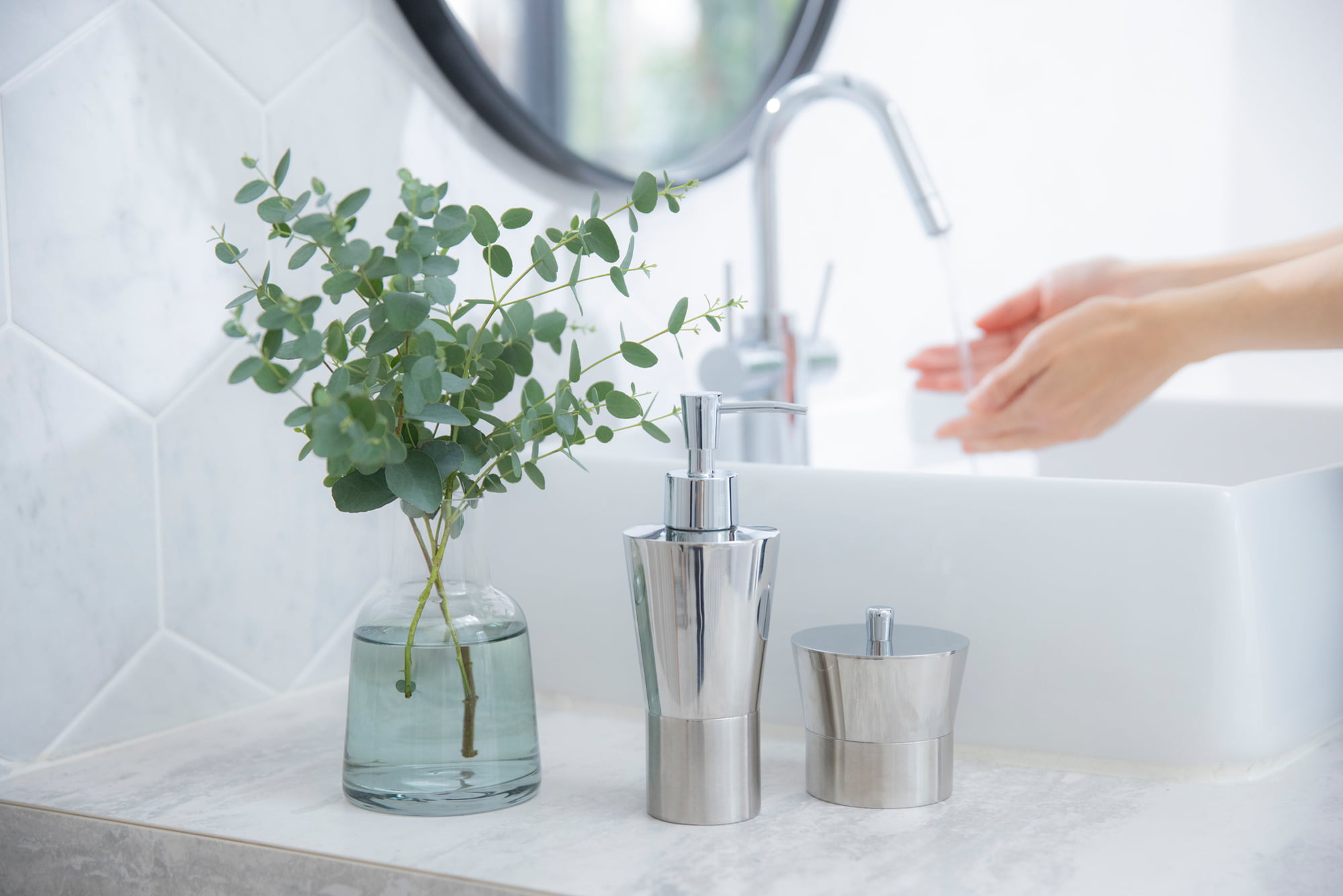 洗面台に並ぶ花瓶とソープディスペンサーのある清潔な洗面室の写真